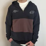 Canguro con capucha y cierre frontal parcial, de diseño color block en negro y marrón. Presenta estampado tipográfico en el pecho derecho y logo bordado en el pecho izquierdo.