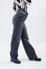 Jean de corte wide leg con tiro alto, en color negro gastado. Presenta un diseño de cinco bolsillos, cierre frontal con botón y cremallera, y trabillas para cinturón.