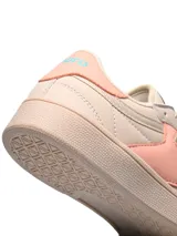 Championes Umbro modelo Rian, de diseño clásico en color blanco con detalles en rosado en el talón y logo lateral. Presentan suela de goma en tono crema y perforaciones en la puntera para mayor ventilación.