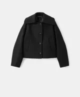 Chaqueta negra de corte corto y holgado, confeccionada con mezcla de lana. Cuenta con cuello ancho y solapa de piel sintética en tono beige claro, cierre frontal con botones oscuros y mangas largas amplias.