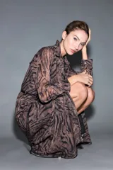 Vestido camisero largo con estampado animal print tipo cebra, en tonos marrón y negro, con cuello camisero, mangas largas y cierre frontal con botones. Incluye un cinturón fino de cordón negro.
