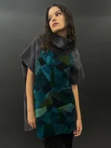 Poncho de lana merino afieltrada con cuello alto y mangas cortas. Diseño tipo mosaico con piezas geométricas en tonos verde azulado y gris.
