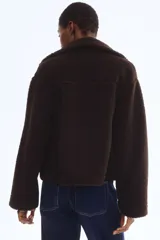 Campera de sherpa color marrón oscuro, con cuello elevado, cierre frontal y bolsillos de parche en los laterales.