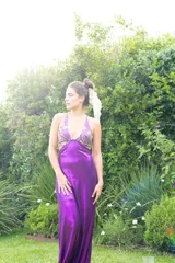 Vestido largo con estampado tie-dye en tonos violeta y fucsia, escote en V con detalles bordados dorados, cut-outs laterales bajo el busto y tirantes finos que se cruzan y atan en la espalda.