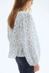 Blusa en mezcla de viscosa con peplum acampanado, cuello redondo, escote en V y tiras finas con cuentas decorativas. Presenta mangas globo largas con elástico en los puños y un estampado en tonos blancos y azules con motivos florales y geométricos.