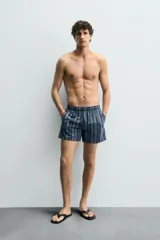 Bañador de hombre de largo medio, color azul claro con rayas verticales en azul oscuro. Posee cintura elástica ajustable con cordón, bolsillos laterales y un bolsillo trasero de plastrón.