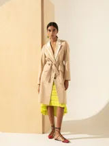 Trench color beige de lino, largo hasta la rodilla, con lazo para ajustar en la cintura y cuello y solapa en lino color crudo. Cierre con botones de carey.