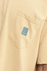 Remera color arena de corte holgado con bolsillo en el pecho y logo estampado en azul.