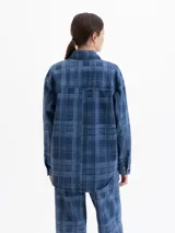 Camisa de denim con diseño a cuadros en tonos azules, cuello clásico, mangas largas y cierre frontal con broches a presión. Presenta bordados florales en el frente y contornos de flores bordados en hilo fino.