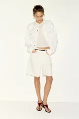 Bermudas de cinco bolsillos en denim de algodón rígido, corte de talle alto con cierre de cremallera y botón, en color blanco.