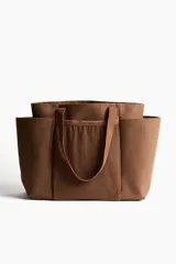 Cartera shopper grande en tejido grueso de mezcla de yute color marrón, con compartimento de malla en el frente y doble asa superior.