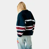 Buzo tipo polo de manga larga con diseño a rayas horizontales en blanco y bordó sobre base azul marino. Presenta el nombre de la marca estampado en el frente y cuello camisero.