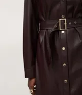 Vestido midi tipo chemise confeccionado en poliuretano, con cuello estructurado, cierre frontal de botones y mangas largas. Incluye un cinturón ajustable con hebilla metálica que marca la cintura.