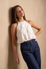 Top halter blanco de viscosa y poliamida, con cuello redondo y diseño sin mangas. Presenta detalles de inserciones de encaje floral formando una cruz en el frente y ruedo fruncido.