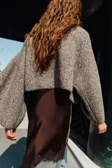Jersey de punto con cuello subido y mangas largas acampanadas. Presenta un diseño envolvente con detalle de bufanda integrada en el mismo tejido y textura jaspeada.