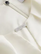 Blusa blanca de poliéster reciclado, con cuello redondo, mangas largas y abertura en el cuello con barra metálica.