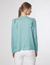 Blusa verde pastel con escote en V, cierre frontal con botones y volados con detalles calados en el frente y las mangas.