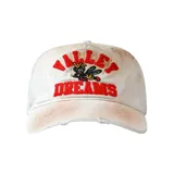 Gorra de béisbol color blanco con efecto desgastado y manchas de color marrón. Presenta un bordado frontal en color rojo con el texto 'VALLEY DREAMS' y un dibujo de una abeja en el centro. Incluye detalles de roturas en el ala.