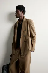 Blazer cruzada de corte relaxed fit, confeccionada en mezcla de algodón color marrón, con solapas de pico, bolsillos de plastrón en la cadera y doble botonadura frontal.