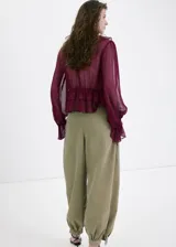 Blusa bordó de tejido fluido y semi transparente, con escote en V pronunciado, mangas largas abullonadas con volantes en los puños y detalles de volantes en el cuello y el ruedo.