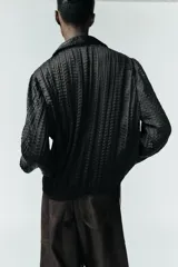 Camisa de manga larga con cuello solapa, confeccionada en tejido satinado con textura efecto arrugado y cierre frontal con botones.