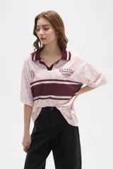 Remera tipo chomba de manga corta con cuello camisero, confeccionada en tejido con estampado de tablero ondulado en tonos rosado y blanco, con franja horizontal y detalles gráficos en color bordó.