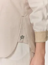 Camisa de lino color blanco con detalles combinados en tonos beige, cuello camisero, cierre frontal con botones oscuros y mangas largas con puños en contraste.