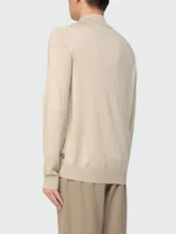 Buzo de punto fino color beige, con cuello alto y cierre frontal parcial, de manga larga y diseño clásico.