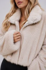 Chaqueta de piel sintética en color beige claro, con diseño corto, cuello amplio y cierre frontal. Presenta una textura suave y un calce relajado.