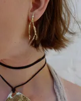 Collar artesanal con dije central de metal con textura orgánica irregular que evoca una ostra. El dije está montado sobre un cordón de algodón natural, permitiendo un uso versátil y regulable.