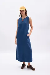 Vestido largo sin mangas de denim azul, con corte recto y holgado, costura central vertical y bolsillos laterales.