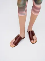 Sandalias planas de cuero color marrón, con diseño minimalista que sujeta el dedo pulgar y deja el empeine al descubierto.