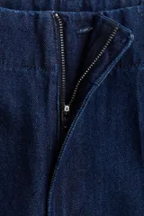 Pantalón de jean tipo wide leg de tiro alto, confeccionado en denim rígido de color azul oscuro. Presenta un corte holgado desde el muslo hasta el ruedo, con raya marcada en el centro de las piernas, cierre con botón oculto y bolsillos al bies.