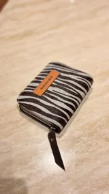 Billetera de cuero de pelo con estampado animal print tipo cebra, con cierre perimetral y tirador de cuero. Incluye una etiqueta de cuero color suela con el logo de la marca grabado.