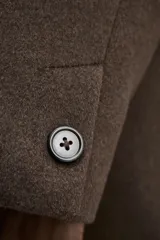 Abrigo marrón de corte recto, con cuello mao y cierre frontal abotonado. Tiene bolsillos laterales y abertura en la parte trasera. Confeccionado en tejido de lana.
