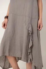 Vestido midi de lino color beige, sin mangas y con cuello redondo. Cuenta con un diseño irregular con detalle de volado vertical a un costado.