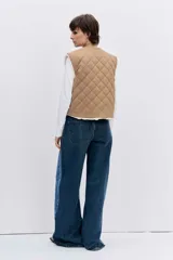 Chaleco reversible de diseño acolchado con costuras en rombos, color tostado con interior de corderito blanco. Presenta cierre frontal con botones, cuello redondo y bolsillos delanteros.