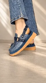 Zuecos cerrados color azul con capellada en cuero de texturas combinadas. Presentan una tira con argolla metálica y remaches en el empeine, y una tira trasera con hebilla regulable. Poseen plataforma y suela de goma color camel.
