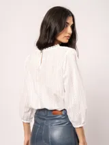 Blusa blanca de algodón con escote redondo, manga tres cuartos y silueta oversized. Presenta bordados y texturas combinadas.