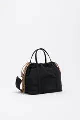 Bolso bandolera pequeño de nylon negro con estructura blanda, doble asa de mano y correa regulable. Cuenta con cierre de cordón ajustable y etiqueta con logo grabado en el frente.