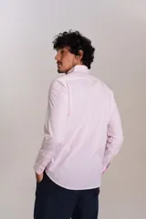 Camisa de manga larga confeccionada en tejido poplin con diseño de rayas verticales finas en color rosado y blanco. Presenta cuello abotonado (button-down), cierre frontal con botones y un bolsillo en el pecho.