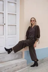 Bota corta de cuero color marrón, con taco cuadrado de madera y punta fina. Presenta una tira decorativa con hebilla metálica dorada alrededor del tobillo.