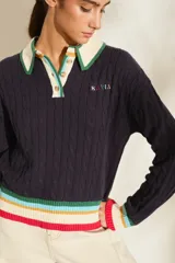 Buzo de punto azul marino con cuello polo blanco y detalles de rayas de colores en el cuello, los puños y el ruedo. Cuenta con cierre frontal parcial de botones y diseño tejido de ochos.