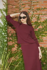 Sweater de tejido de punto en color bordó, con cuello redondo y mangas largas. Presenta un diseño de corte recto y textura acanalada.