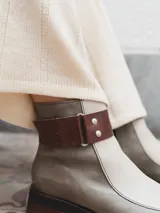 Bota corta de cuero color gris y beige, con detalle de correa marrón con hebilla y tachas plateadas. Tiene suela de goma negra y taco de madera.