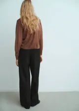 Cardigan de punto fino color marrón, con cuello en pico, cierre frontal con botones y detalle de fular integrado en el cuello. De diseño recto y manga larga.