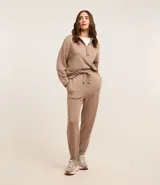 Conjunto de dos piezas color beige, compuesto por un sweater de manga larga con cuello polo y cierre frontal parcial, y un pantalón jogger a juego con cordón ajustable en la cintura.