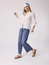 Blusa blanca de algodón con bordado calado, escote en V con lazos, mangas largas con volados en los puños y corte holgado.