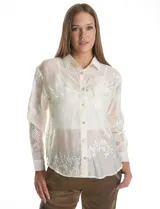 Camisa de tencel color blanco roto, semitransparente, con bordados florales en blanco. Tiene cuello con solapa, cierre frontal con botones decorados y un bolsillo en el pecho.