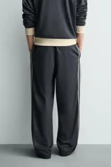 Pantalón jogger de corte wide fit en tejido compacto color gris oscuro. Presenta cintura elástica con cordón ajustable, bandas laterales en contraste color beige y costuras frontales tipo pinza.